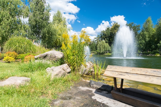 Panchina in un parco che si affaccia su fontane ornamentali in un lago circondato da alberi frondosi in un paesaggio panoramico