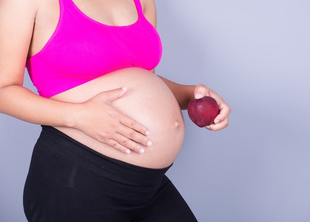 pancia del primo piano della donna incinta con la mela rossa su fondo grigio