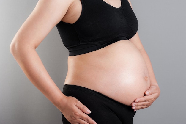 Pancia del primo piano della donna incinta sopra fondo grigio