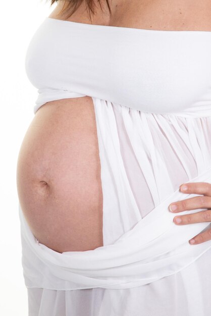 Pancia della pancia della donna incinta su sfondo bianco in camicia bianca aperta