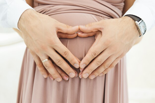 Pancia delle mani di una ragazza incinta a forma di cuore