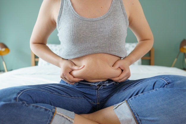 Pancia grassa del corpo delle donne. Mano di donna obesa che tiene il grasso della pancia eccessivo.