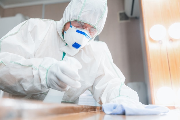 Pandemia di coronavirus. Un disinfettante in una tuta protettiva e una maschera spruzza disinfettanti in casa o in ufficio. Protezione contro la malattia COVID-19. Prevenzione della diffusione del virus della polmonite con le superfici.