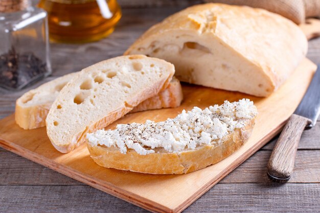 Pane a fette appena sfornato sul tagliere di legno con ricotta, ciabatta