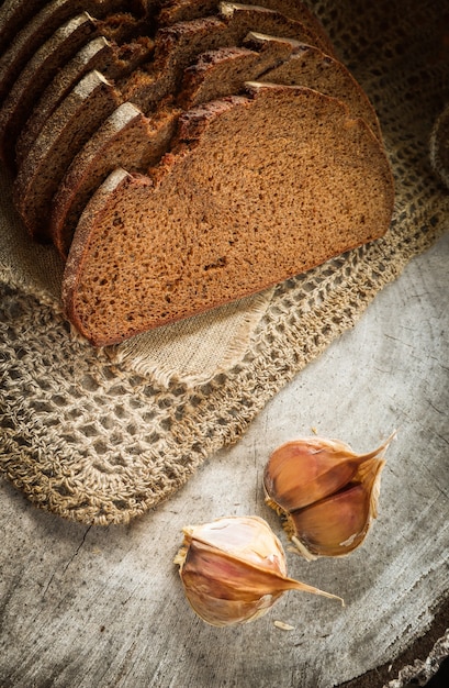 Pane a fette di segale fresco su tovagliolo di lino naturale e spicchi d'aglio su fondo di legno rustico