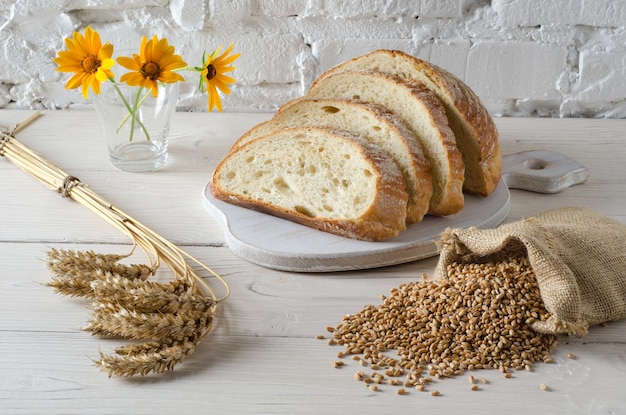 Pane a fette su tagliere e piccola borsa con chicco di grano sul tavolo di legno bianco. Stile rustico.