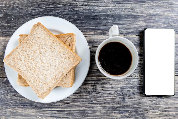 Pane affettato sul piatto e tazza di caffè con un telefono cellulare con uno schermo vuoto