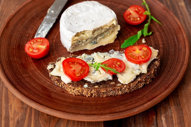 Pane ai cereali con gorgonzola e pomodorini su un piatto di argilla su uno sfondo di legno. Cibo vegetariano sano.