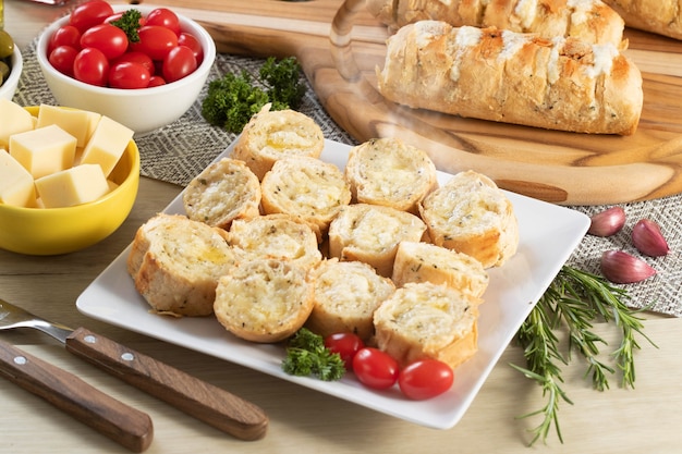 Pane all'aglio in piatto quadrato bianco sul tavolo con formaggio, rosmarino, olive e pomodorini.