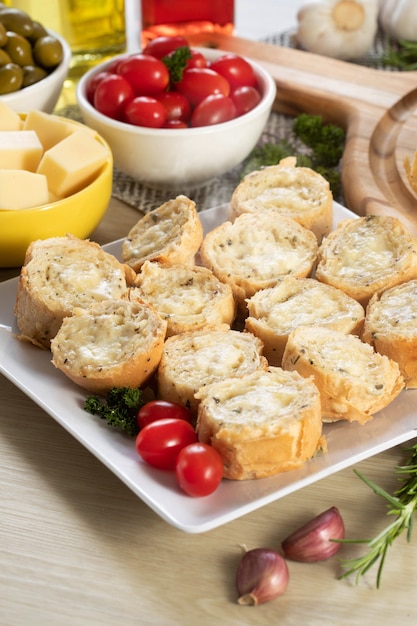 Pane all'aglio in piatto quadrato bianco sul tavolo con formaggio, rosmarino, olive e pomodorini.