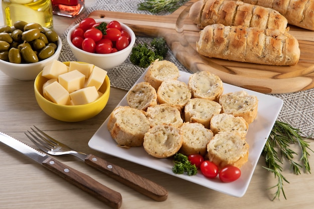 Pane all'aglio in piatto quadrato bianco sul tavolo con formaggio, rosmarino, olive e pomodorini.