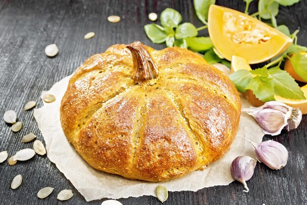 Pane alla zucca su pergamena, aglio, basilico, pezzi e semi di una verdura su un fondo di legno