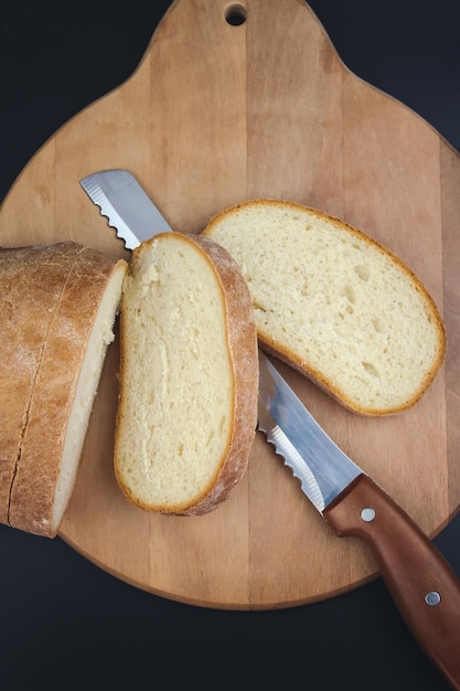 Pane appena sfornato affettato con un coltello da pane seghettato su un tagliere di legno