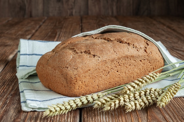 Pane appena sfornato con un asciugamano da cucina e orecchie su uno sfondo di legno rustico