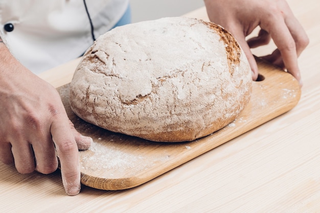 Pane appena sfornato su una tavola di legno nelle mani di un fornaio. luce soffusa