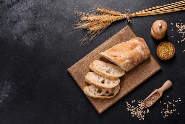 Pane baguette francese affettato su un tagliere di legno su uno sfondo di cemento scuro