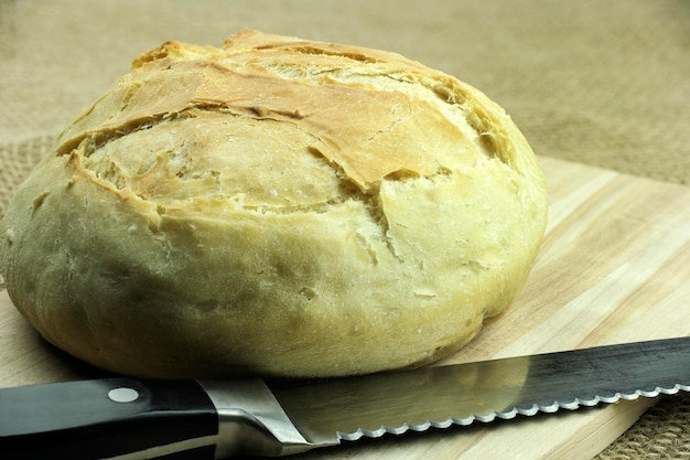 Pane bianco appena cotto con farina bianca su una tavola da taglio e un coltello per tagliare il pane a tutta profondità
