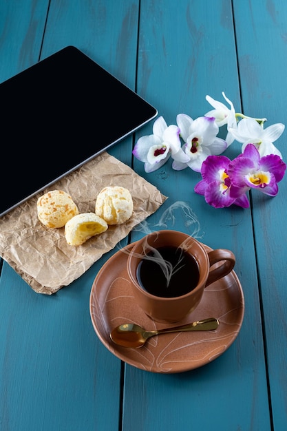 Pane brasiliano al formaggio accanto alla compressa dorata del cucchiaio della tazza di caffè e ai flowersvertical