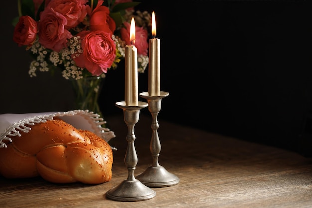 Pane Challah coperto con un tovagliolo speciale e due candele accese sul tavolo di legno Rituale tradizionale Shabbat ebraico Shabbat Shalom