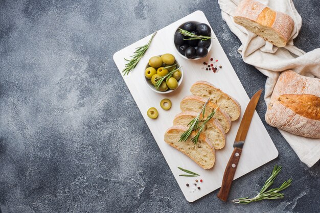 Pane ciabatta italiana con olive e rosmarino su un tagliere Sfondo concreto scuro