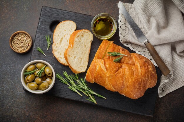 Pane ciabatta tradizionale italiano con olive, olio d'oliva, pepe e rosmarino su una superficie di pietra o cemento scuro