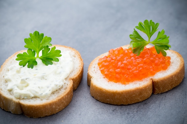 Pane con crema di formaggio fresca e caviale rosso sul tavolo.