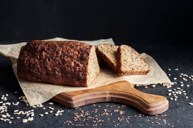 Pane con semi di girasole e lino su un tagliere di legno su fondo nero