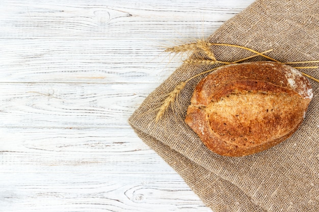 Pane delizioso pane di grano intero sulla superficie in legno bianco con grano secco, vista dall&#39;alto