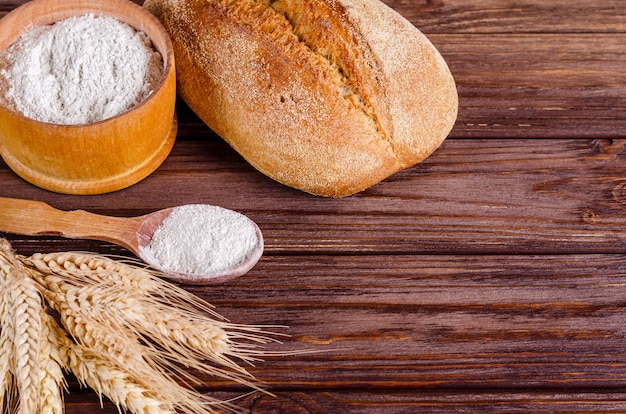 Pane di segale, farina e spighette su uno sfondo di legno.