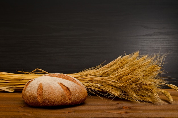 Pane di segale rotondo e un covone sulla tavola di legno, fondo nero, spazio per testo