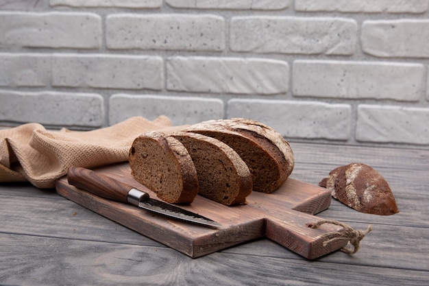 Pane di segale tondo pagnotta tagliata a pezzi su una tavola di legno con un coltello in legno rustico.