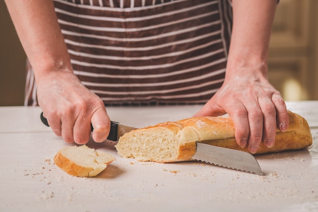 Pane di taglio della donna sulla tavola di legno. Forno. Produzione di pane. Una donna con un grembiule a righe