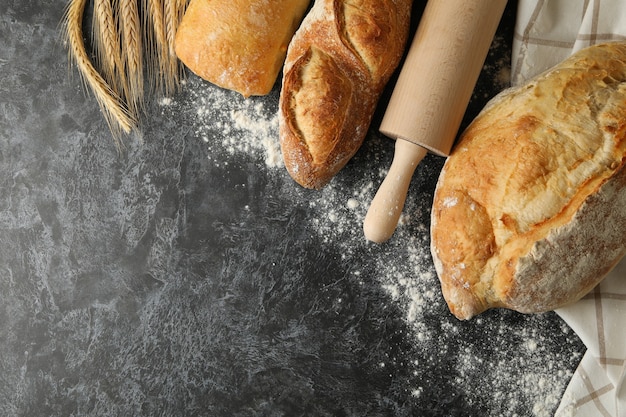 Pane diverso, spighette e mattarello su sfondo nero smokey