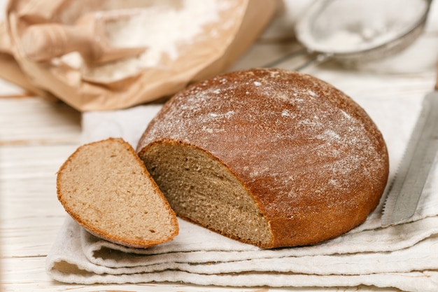 Pane fatto in casa appena sfornato, farina e un coltello su un vecchio tavolo di legno