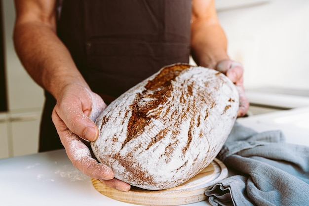 Pane fatto in casa artigianale di segale nelle mani muscolose e testurizzate del panettiere maschio