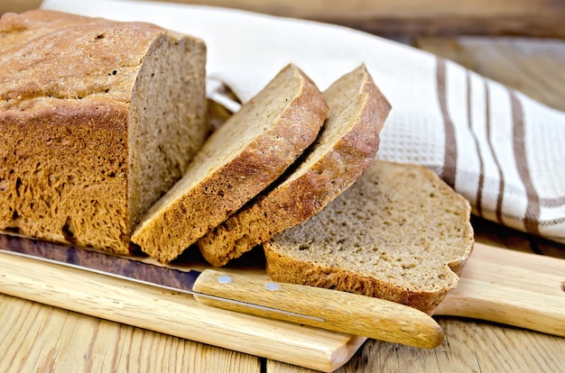 Pane fatto in casa di segale affettato con un coltello e un tovagliolo sullo sfondo di tavole di legno