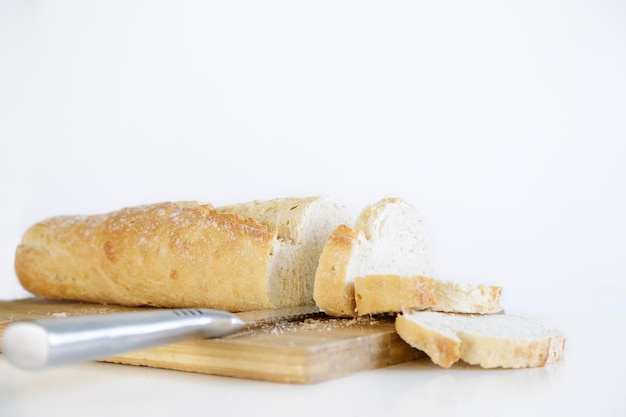 Pane francese tagliato a fette su tagliere di legno su sfondo bianco con spazio di copia