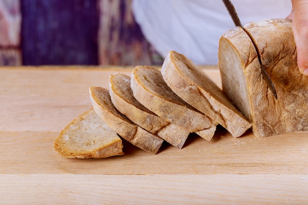 Pane fresco del grano intero sul tavolo da cucina o sul coltello e sul taglio di pane della tenuta dell&#39;uomo di legno del pane