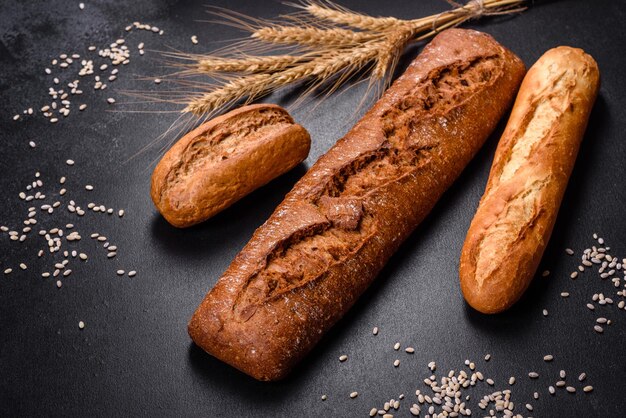 Pane fresco su sfondo nero, vista dall'alto, copia spazio. Varie pagnotte di grano e pane di segale fatte in casa appena sfornate