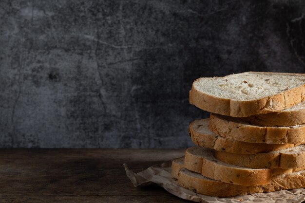 Pane integrale a fette di grano su fondo di legno rustico scuro, ingredienti bio, cibo sano.