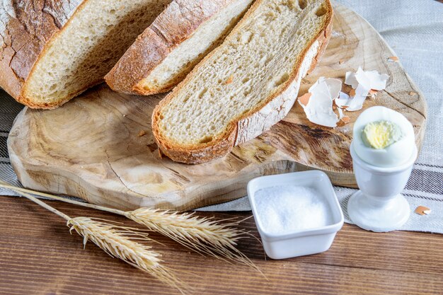 Pane integrale a fette, spighette di grano, sale e uovo sul tavolo della cucina. Cibo sano per la colazione.