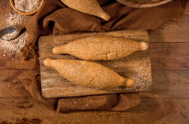 Pane integrale, baguette su legno rustico con pentola di farina integrale sullo sfondo. vista dall'alto