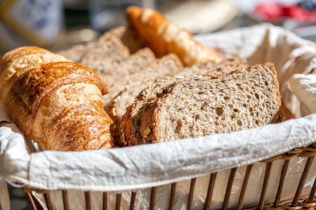 Pane integrale e croissant neri affettati in un cestino. Avvicinamento.