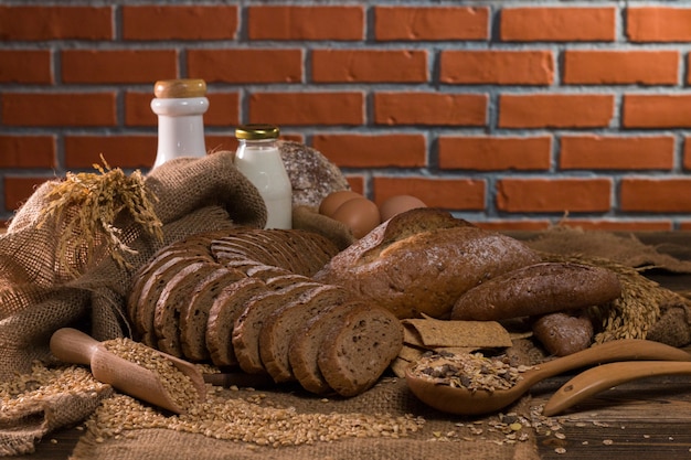 Pane integrale, latte, farina e sacchetto di stoffa sul tavolo di legno.