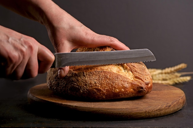 Pane integrale messo su un piatto di legno da cucina con uno chef che tiene un coltello per tagliare Pane fresco sul primo piano del tavolo Pane fresco sul tavolo della cucina Il concetto di alimentazione sana e panetteria tradizionale