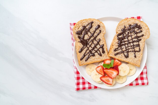 Pane integrale tostato con banana fresca, fragola e cioccolato per colazione