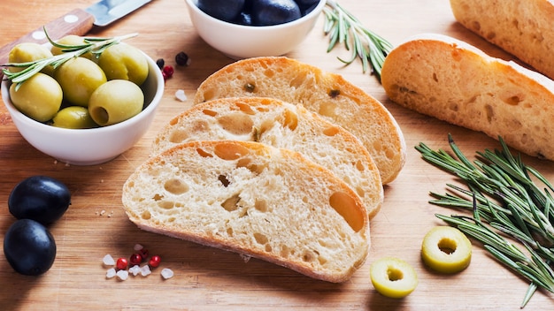 Pane italiano di ciabatta con olive e rosmarino su una tavola di legno.