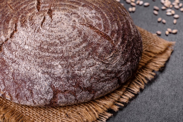 Pane marrone fatto in casa appena sfornato su uno sfondo di cemento nero con chicchi di grano