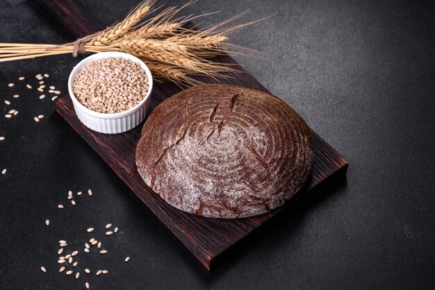 Pane marrone fatto in casa appena sfornato su uno sfondo di cemento nero con chicchi di grano