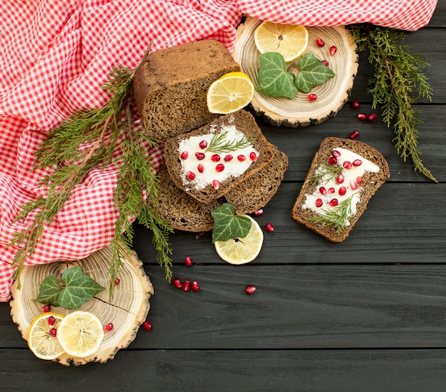 Pane nero con granate bacche su un fondo in legno nero. Alimento di Natale, decorazioni natalizie con limone, ginepro, ramo, bacche rosse